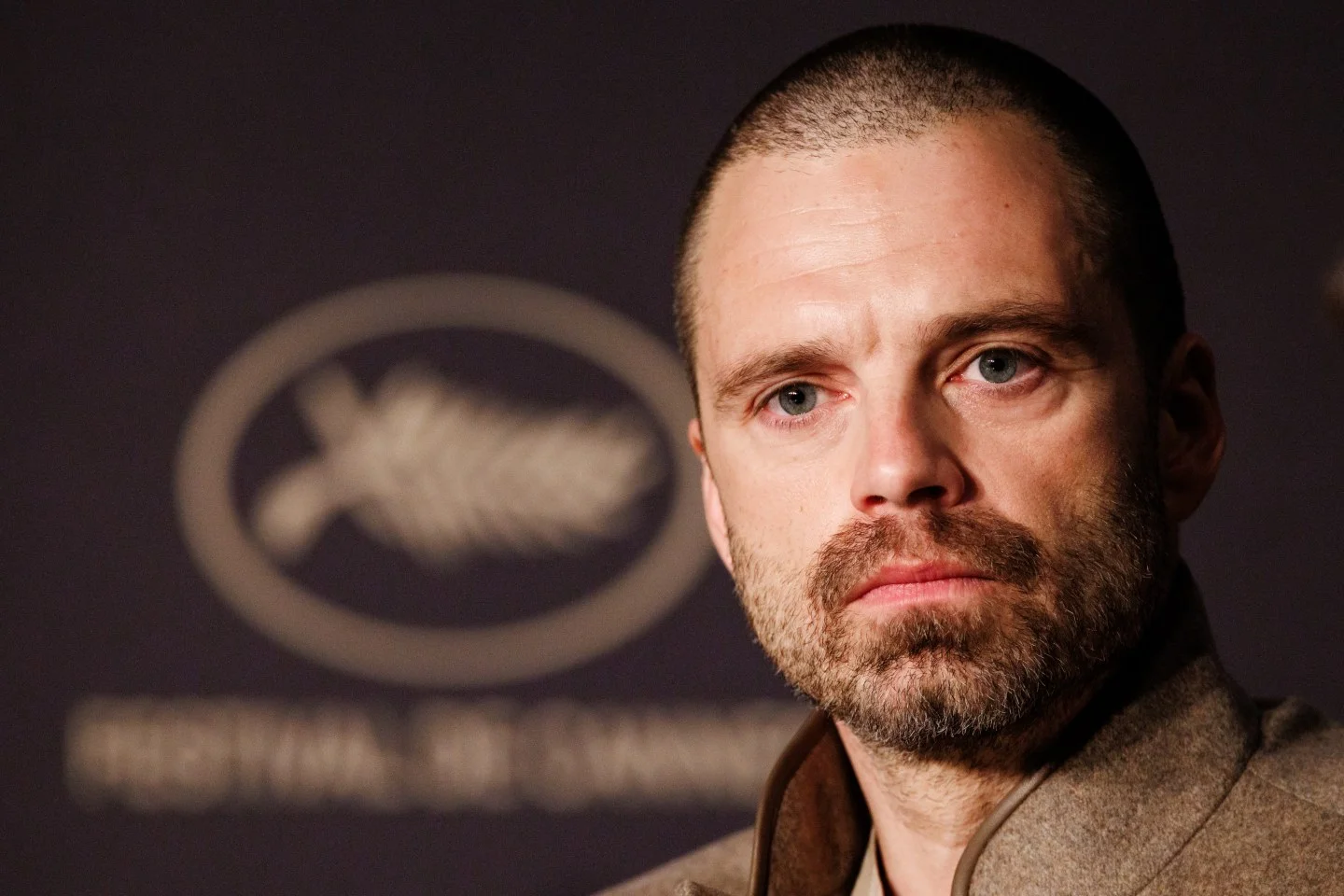 Sebastian Stan en conférence de presse à Cannes 2026, barbe et regard fermé devant le logo du Festival