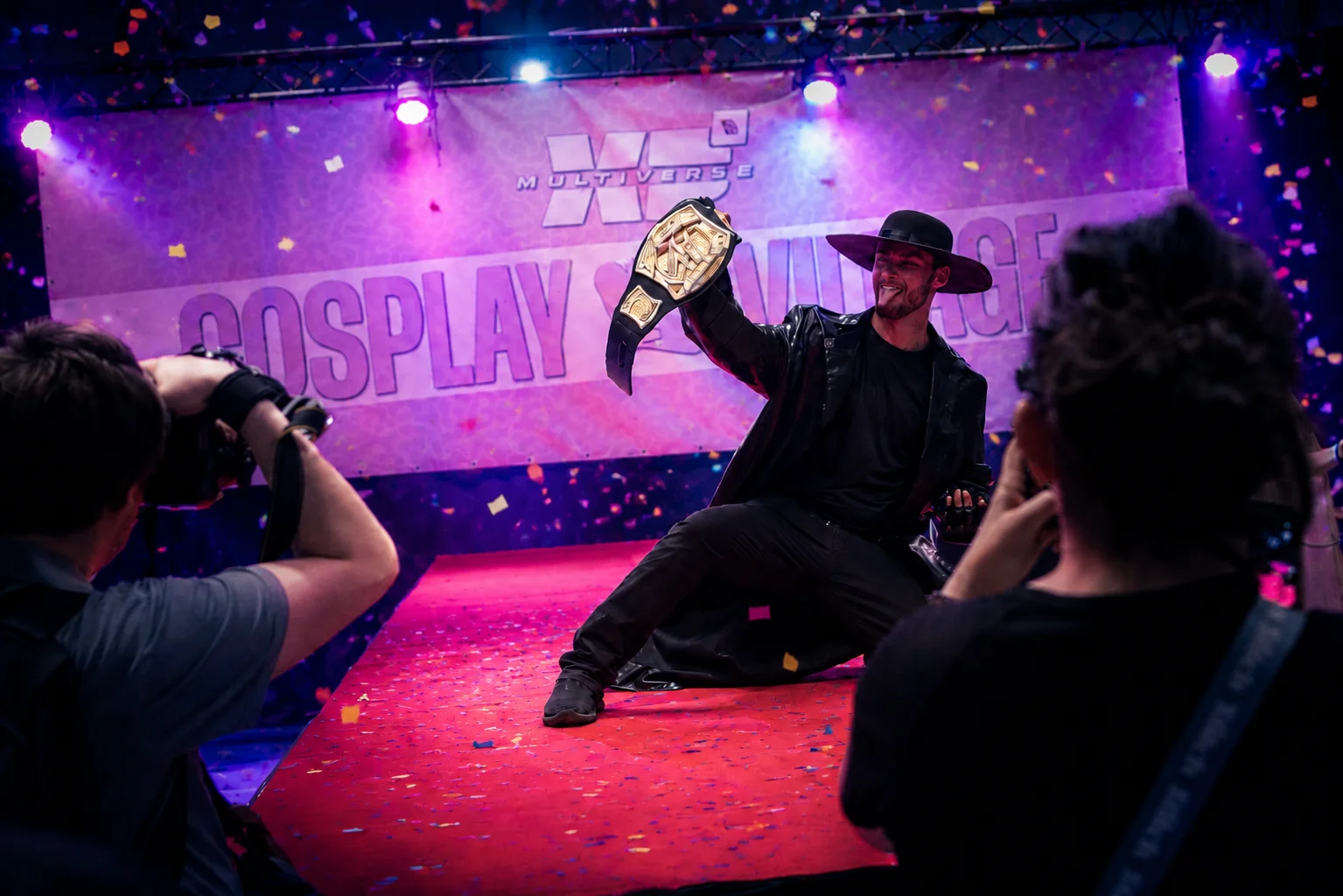 Un cosplayer brandit son trophée sur la scène du Cosplay Challenge de XP Multiverse Tournai, sous les confettis