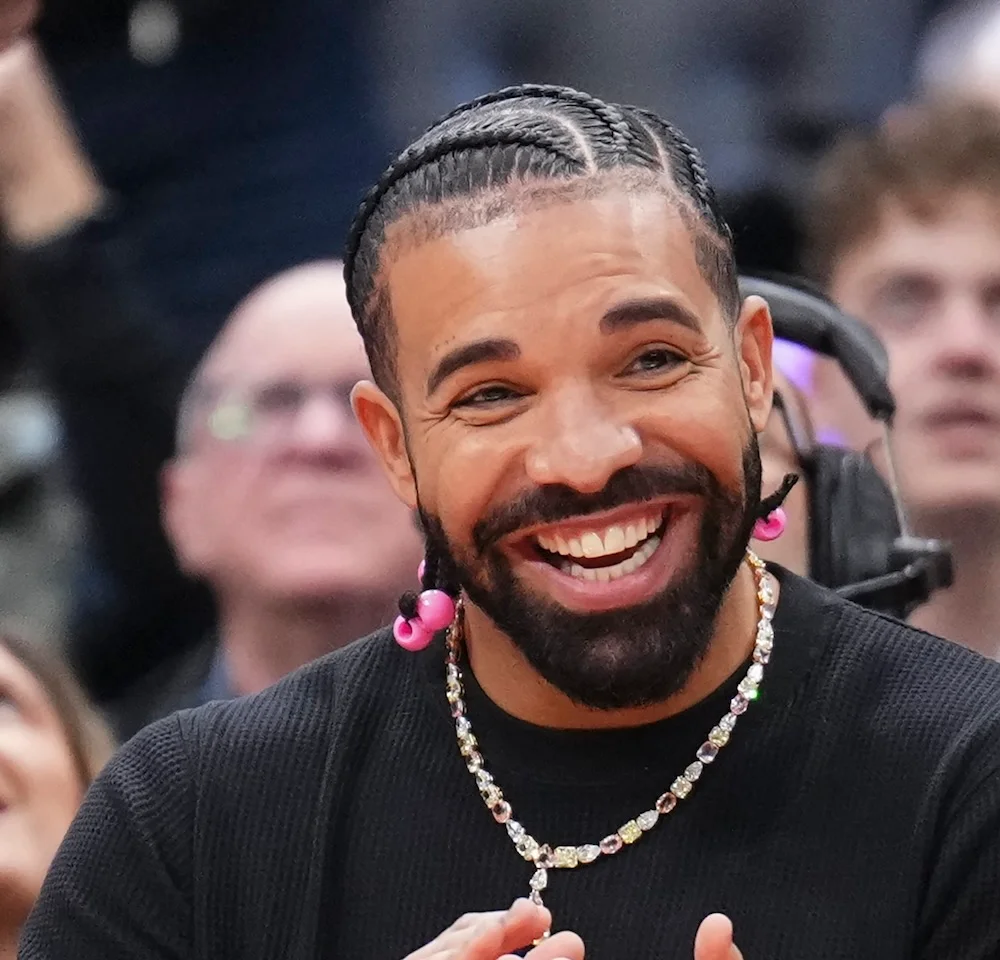 Drake souriant en bord de terrain, chaîne en diamants, lors d'un match de basket