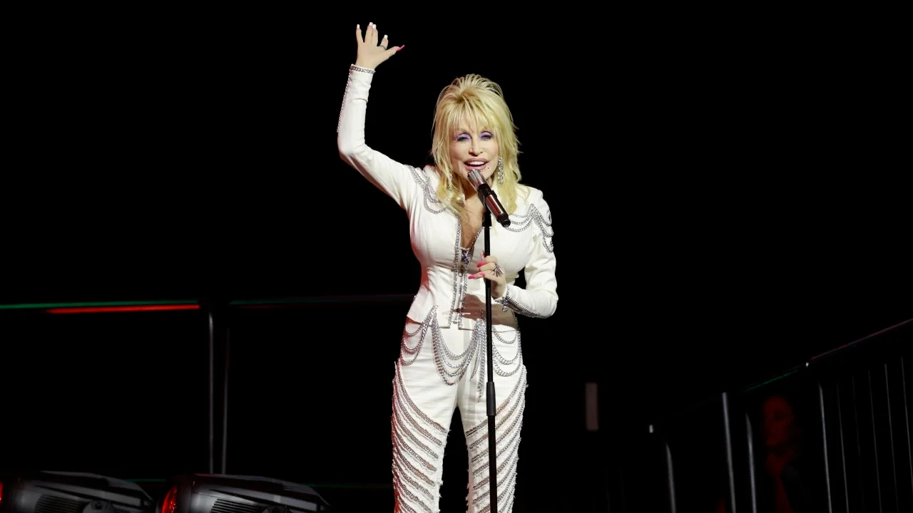 Dolly Parton sur scène ces dernières années, en combinaison blanche à strass, saluant le public