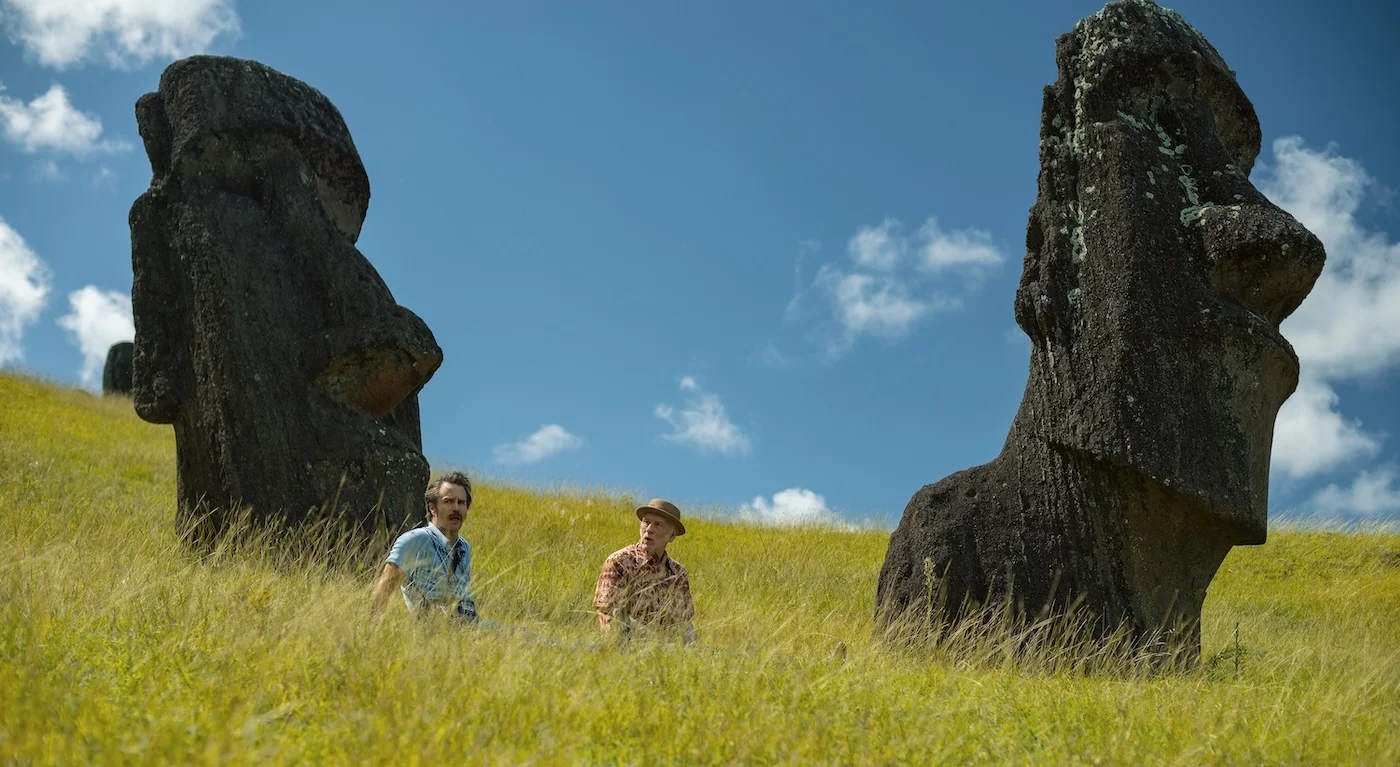 Sam Rockwell et John Malkovich assis dans les herbes hautes de l'île de Pâques, entre deux moaï, dans une scène de Wild Horse Nine