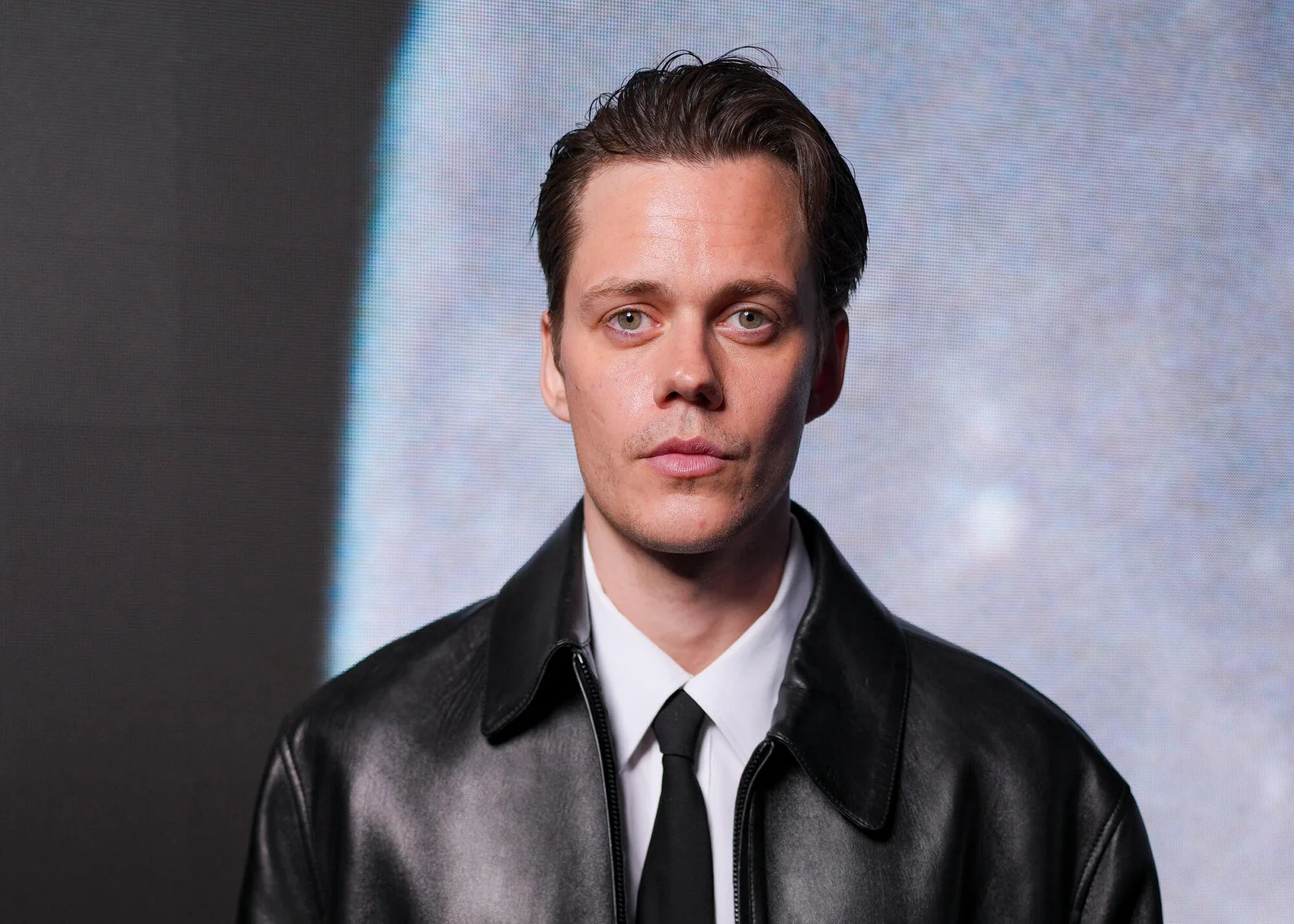 Bill Skarsgård en veste de cuir noire et cravate, sur un tapis rouge