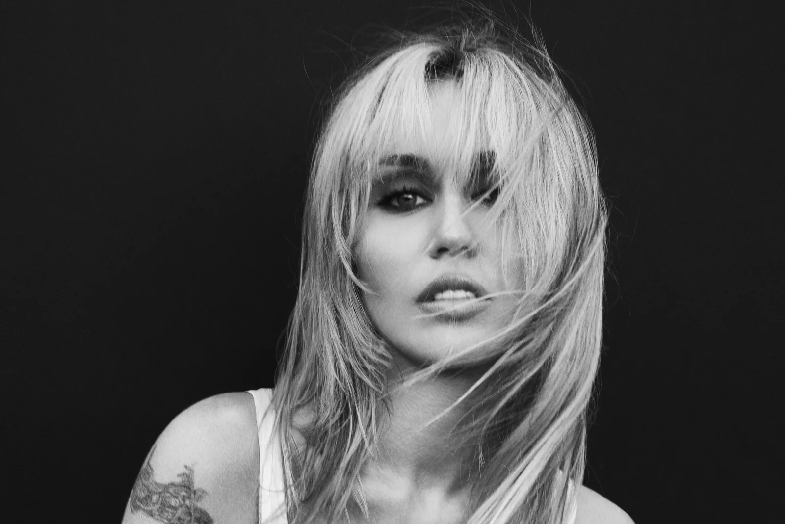 Portrait en noir et blanc de Miley, cheveux dans le visage, sur fond sombre
