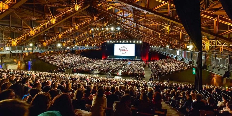 La Halle Tony Garnier remplie de spectateurs sous sa charpente métallique, avec le logo du Festival Lumière à l'écran