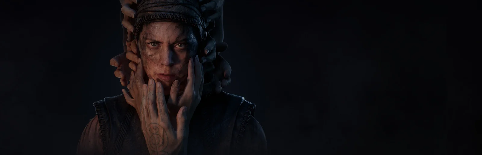 Senua, l'héroïne de Hellblade II: Senua's Saga, le visage enserré par des mains, dans le jeu de Ninja Theory