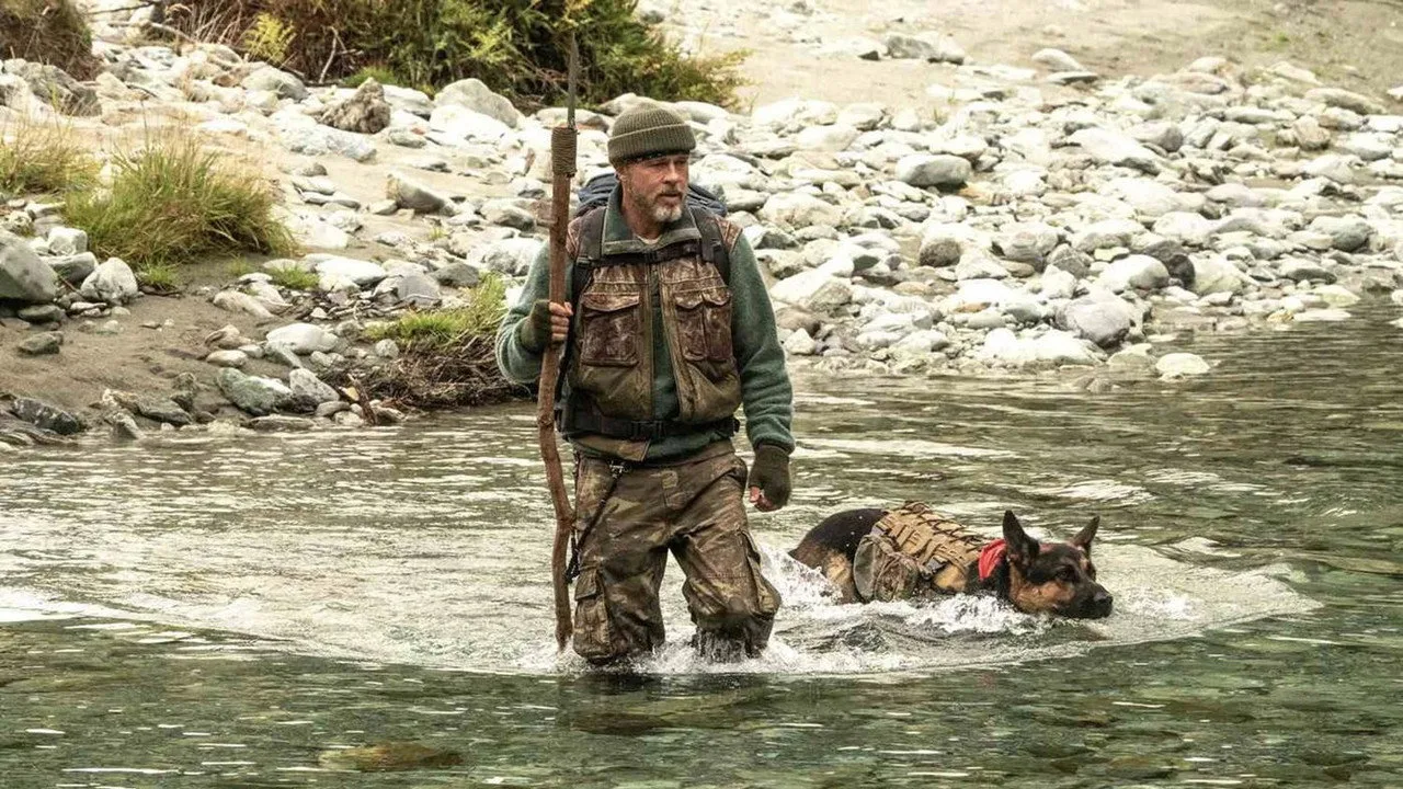 Brad Pitt traverse une rivière à gué, un bâton à la main, suivi de son berger allemand Odin qui nage à ses côtés